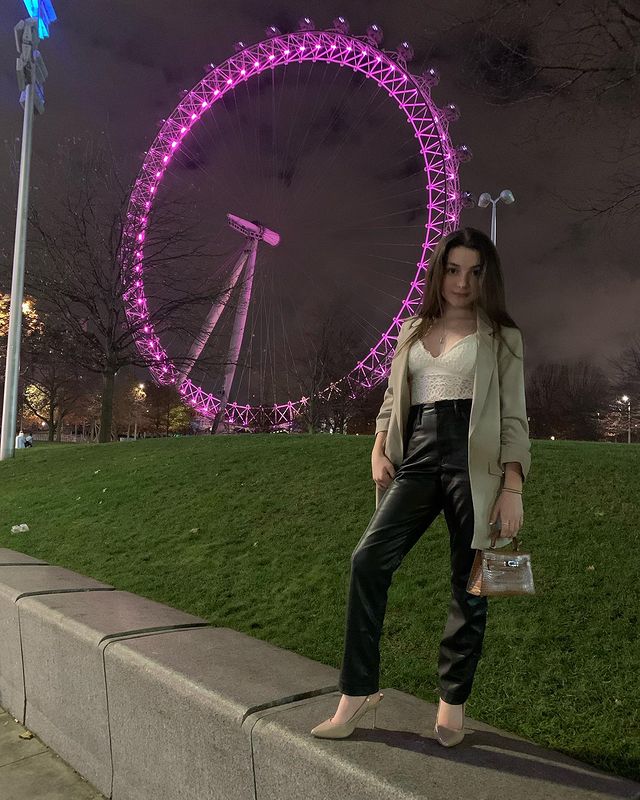 Lilly Aspell in a random park wearing black pant, white vest and White coat holding silver bag