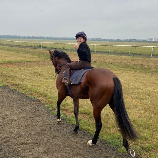 Lilly Aspell in the barn wearing a helmet, black shirt and brown pant training horse riding