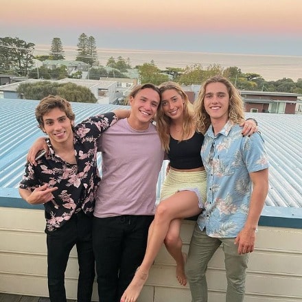 Kai Lewins posing with his friends by wearing light blue t-shirt and fade green pant.