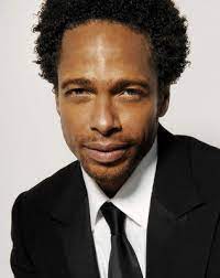 Photo of Gary Dourdan wearing a black coat, tie and a white shirt.
