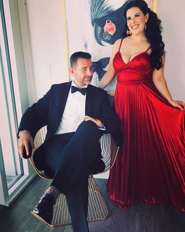 Alexis is wearing red gown and David is wearing black suit with shirt with black bow.