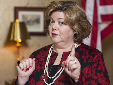 Picture of Catherine Disher pointing her finger to the camera wearing red dress and white necklace