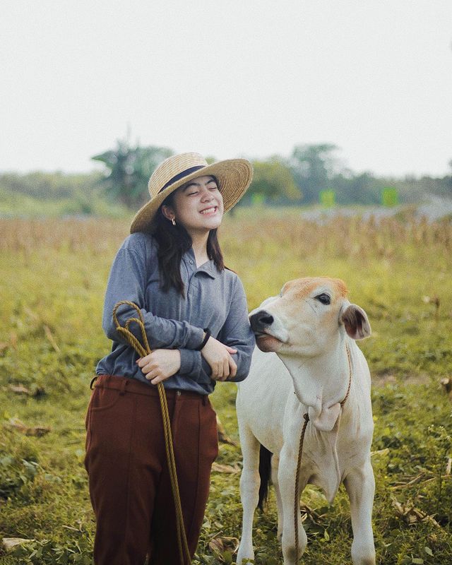 Niana Guerrero posing for the picture with the cow wearing hat and with a  little bit smile on her face