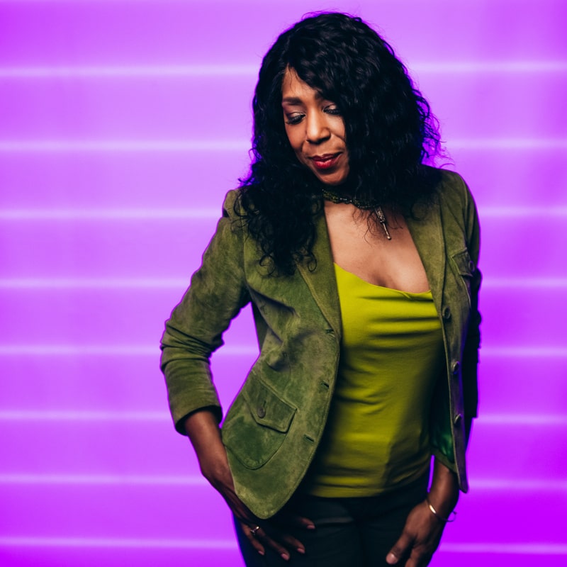 Dawnn Lewis wearing  green t-shirt and brown outer with a long ear ring and short black hair