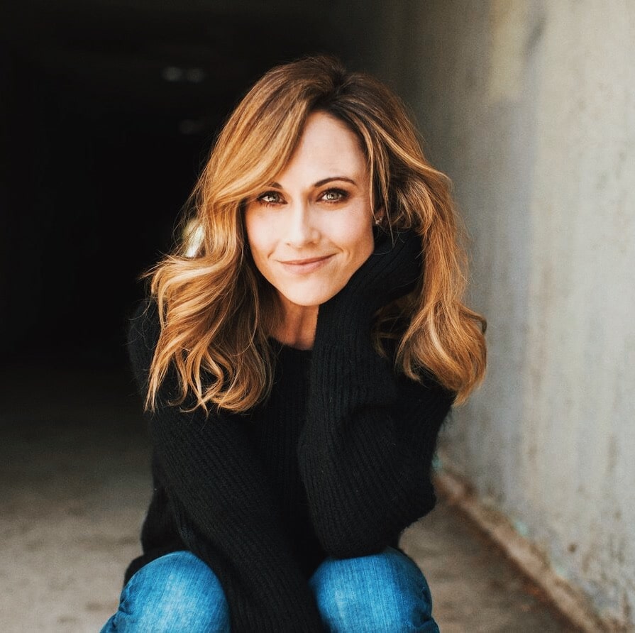Nikki DeLoach posing for the picture siiting in a floor with a smiley face and dark brown hair.