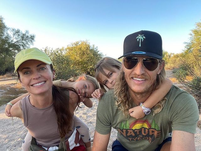 Picture of Tyson Apostol with his wife Rachel Foulger and daughters posing for a photoshoot wearing brown color t shirt and black cap