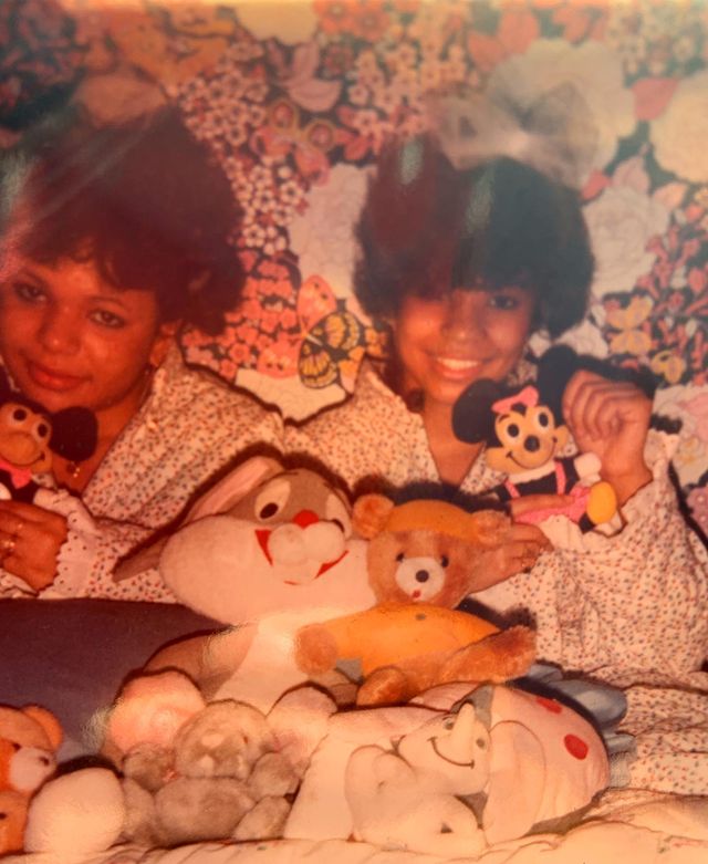 Childhood picture of Kaila Chambers posing for a photoshoot with her toys wearing white color dress