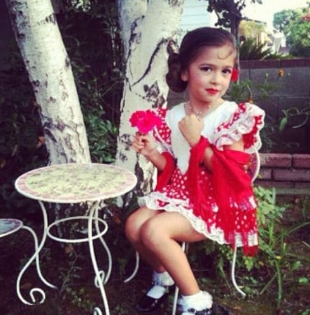 Photo of Maria Canal-Barrera in her childhood  in red dress sitting on a chair in a garden